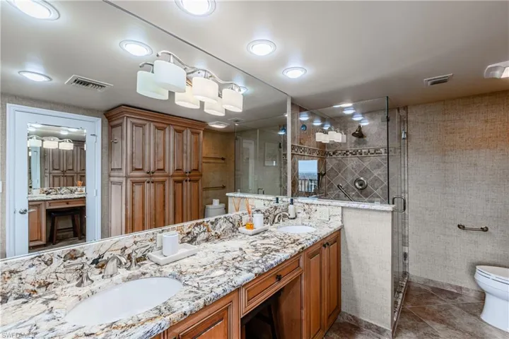 Bathroom with toilet, tile patterned floors, tile walls, dual bowl vanity, and a shower with shower door