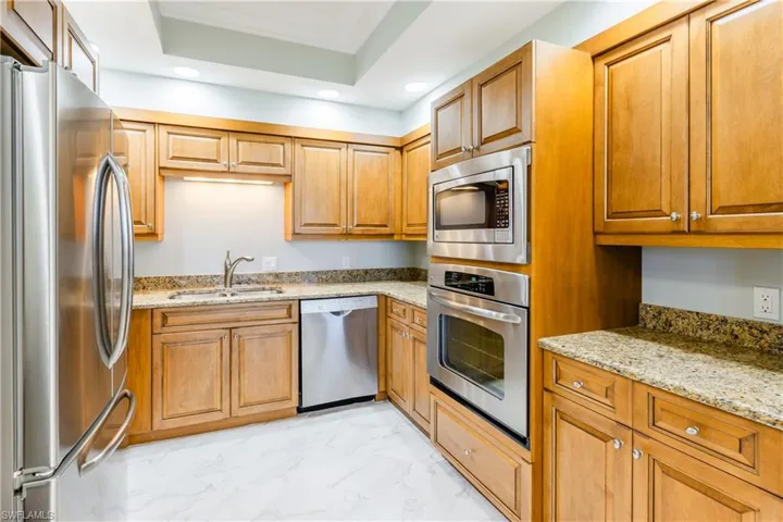 Kitchen featuring sink, appliances with stainless steel finishes, light stone countertops, a tray ceiling, and light tile patterned floors