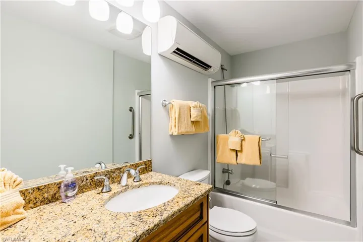 Full bathroom with vanity, toilet, an AC wall unit, and enclosed tub / shower combo