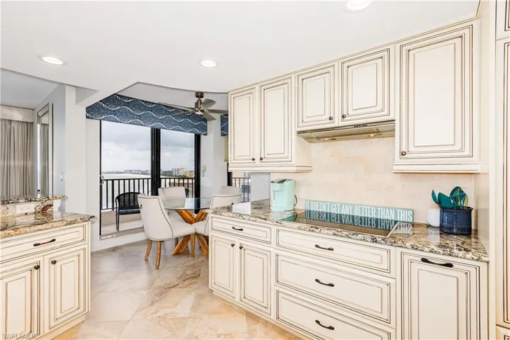 Kitchen with ceiling fan, black electric stovetop, light stone countertops, cream cabinetry, and light tile patterned floors