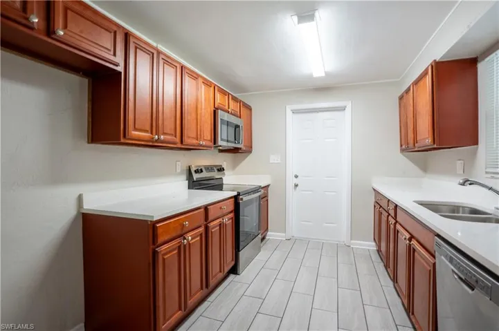 Kitchen with appliances with stainless steel finishes, light stone counters, and brown cabinets