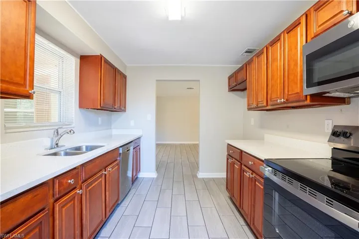 Kitchen featuring appliances with stainless steel finishes, light stone counters, and brown cabinets