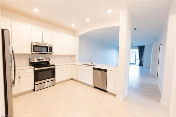 Kitchen with stainless steel appliances, white cabinets, light tile patterned floors, and recessed lighting