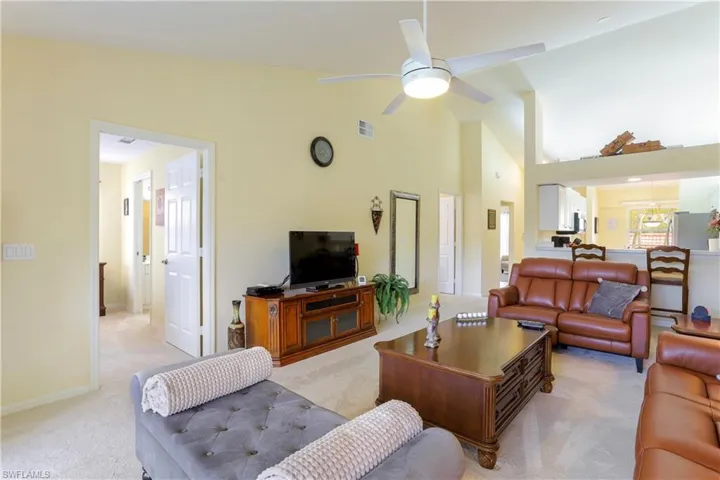 Carpeted living room with ceiling fan and high vaulted ceiling