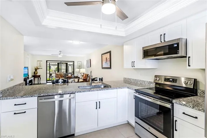 Kitchen with ceiling fan, a tray ceiling, white cabinetry, stone countertops, and appliances with stainless steel finishes