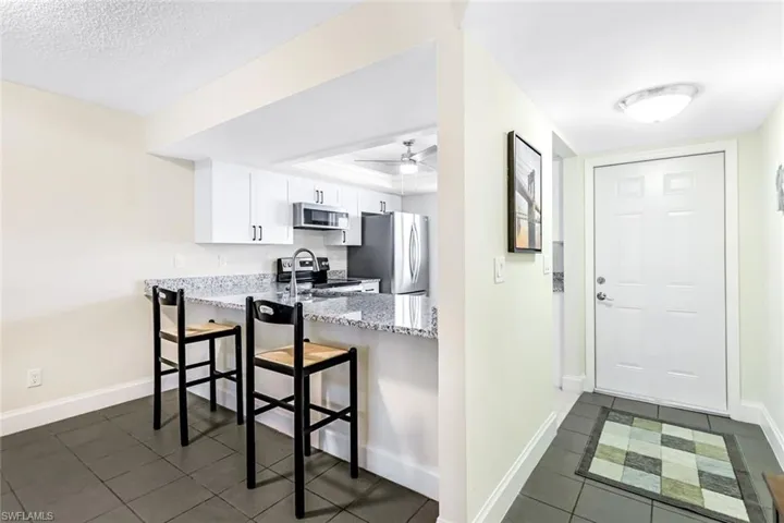 Kitchen with appliances with stainless steel finishes, dark tile patterned floors, light stone countertops, a textured ceiling, and white cabinets