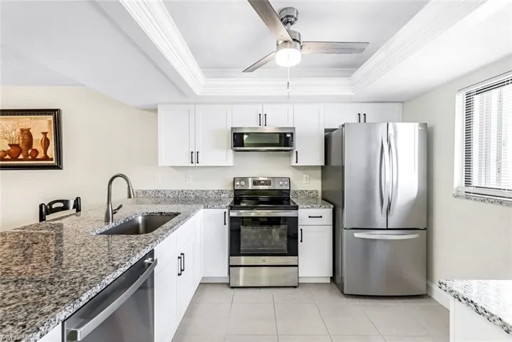 Kitchen with stainless steel appliances, sink, white cabinets, a tray ceiling, and ceiling fan