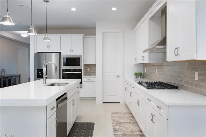 Kitchen with an island with sink, hanging light fixtures, white cabinetry, stainless steel appliances, and light stone counters