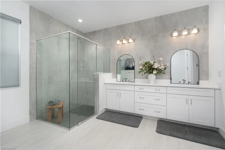 Full bathroom with double vanity, a shower stall, wood finish floors, and recessed lighting