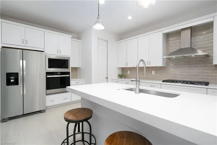 Kitchen with stainless steel appliances, hanging light fixtures, wall chimney range hood, white cabinetry, and recessed lighting