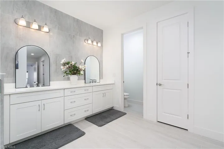 Bathroom featuring double vanity, tile walls, and light wood-style floors