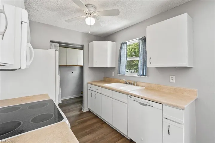 Kitchen with white appliances, a textured ceiling, dark wood-style flooring, white cabinetry, and light countertops