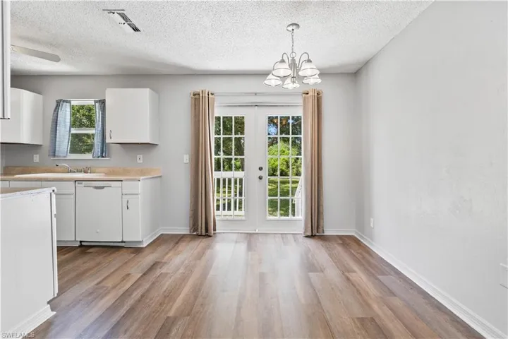 Kitchen with light countertops, light wood-style flooring, french doors, white cabinets, and a chandelier