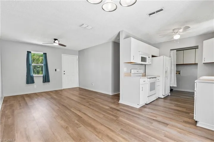Kitchen with ceiling fan, white appliances, a textured ceiling, and light wood-style floors