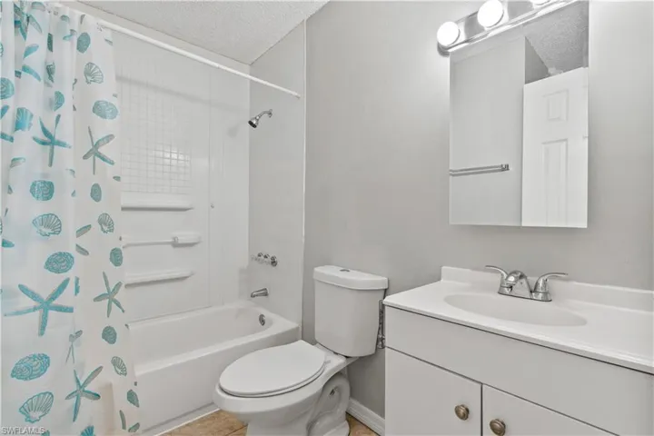 Bathroom with shower / bath combination with curtain, a textured ceiling, and vanity