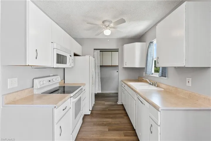 Kitchen with white appliances, a ceiling fan, a textured ceiling, white cabinets, and light countertops