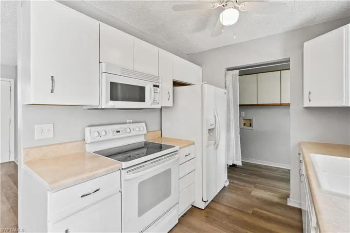 Kitchen featuring white appliances, a textured ceiling, light countertops, ceiling fan, and white cabinets