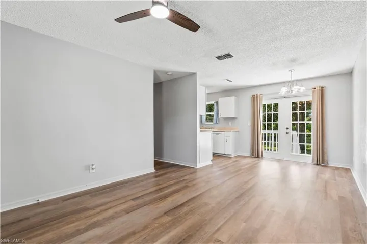 Unfurnished living room with ceiling fan, french doors, light wood-style floors, a textured ceiling, and a chandelier