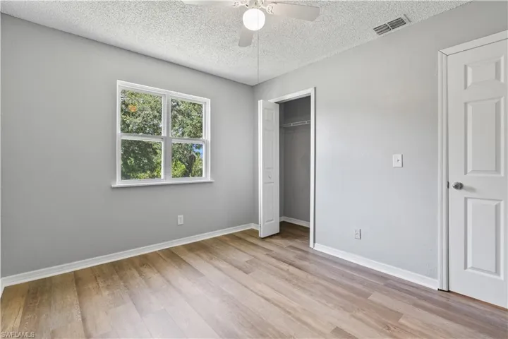 Unfurnished bedroom with light wood-type flooring, a textured ceiling, a closet, and a ceiling fan