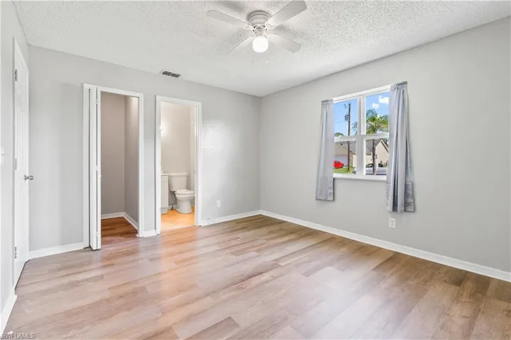 Unfurnished bedroom with light wood-style flooring, a textured ceiling, a ceiling fan, and ensuite bath