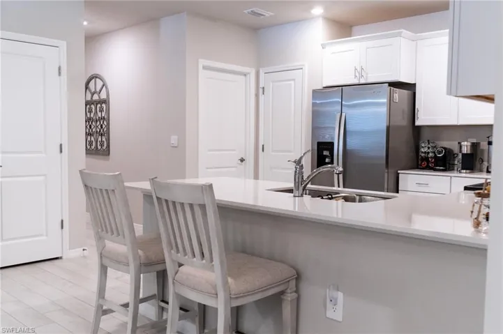 Kitchen with stainless steel fridge with ice dispenser, sink, white cabinets, kitchen peninsula, and a kitchen bar