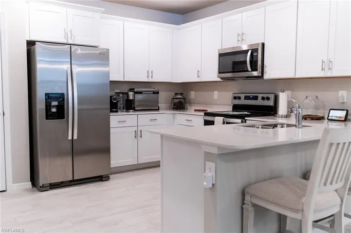 Kitchen with light hardwood / wood-style flooring, stainless steel appliances, a kitchen bar, and white cabinetry