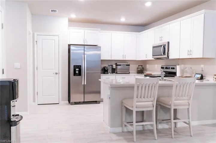 Kitchen with a kitchen breakfast bar, white cabinets, kitchen peninsula, stainless steel appliances, and light hardwood / wood-style flooring