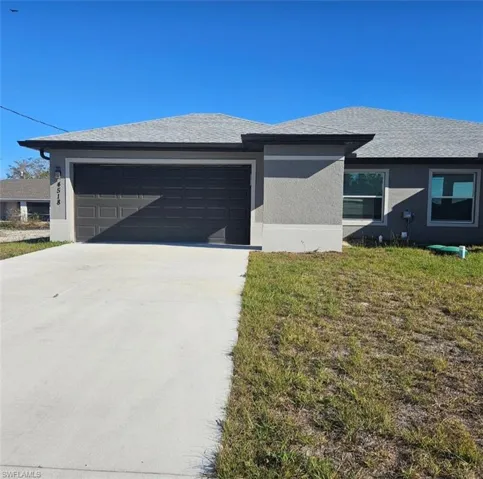 View of front of property with stucco siding, concrete driveway, an attached garage, and a front lawn