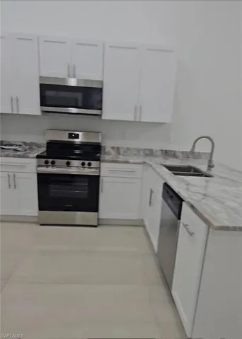 Kitchen with stainless steel appliances, white cabinetry, light stone countertops, and a peninsula