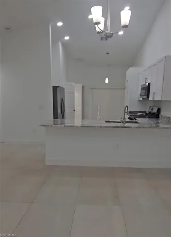 Kitchen featuring light stone counters, a peninsula, white cabinetry, stainless steel appliances, and light tile patterned floors