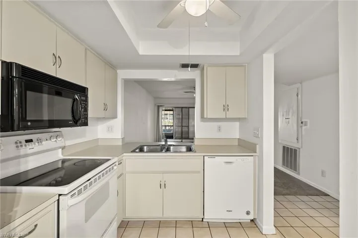 Kitchen with white appliances, light countertops, a tray ceiling, a ceiling fan, and light tile patterned flooring