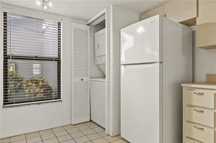 Kitchen with freestanding refrigerator, cream cabinetry, stacked washer / dryer, light countertops, and light tile patterned floors