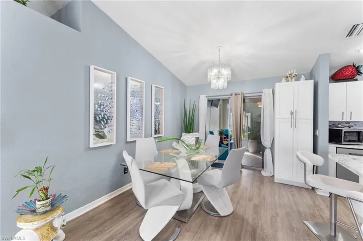 Dining area featuring light wood-type flooring, a notable chandelier, and vaulted ceiling