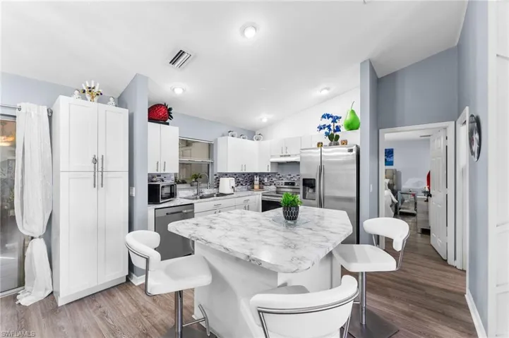Kitchen with lofted ceiling, a breakfast bar area, hardwood / wood-style flooring, and stainless steel appliances