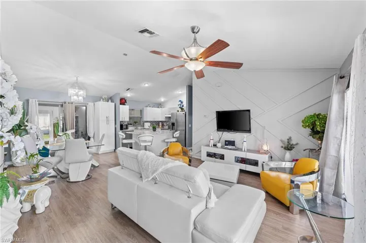 Living room featuring ceiling fan with notable chandelier, vaulted ceiling, and light hardwood / wood-style flooring