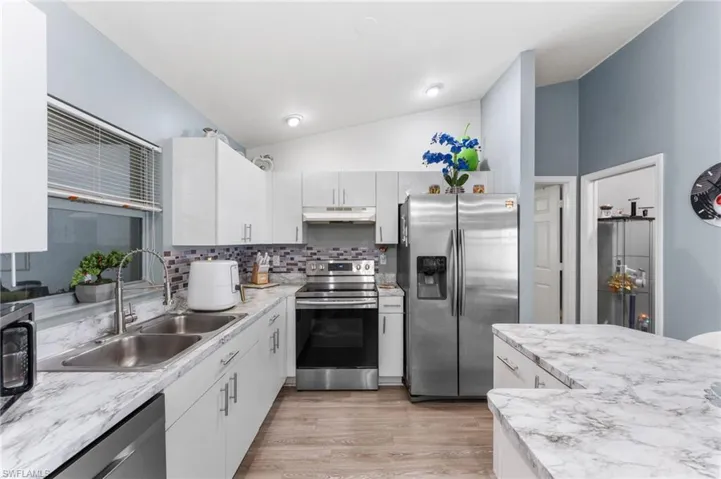 Kitchen featuring stainless steel appliances, sink, white cabinets, light wood-type flooring, and vaulted ceiling