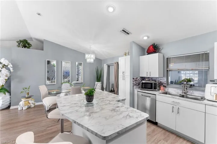 Kitchen featuring stainless steel appliances, a kitchen island, white cabinetry, light hardwood / wood-style floors, and lofted ceiling
