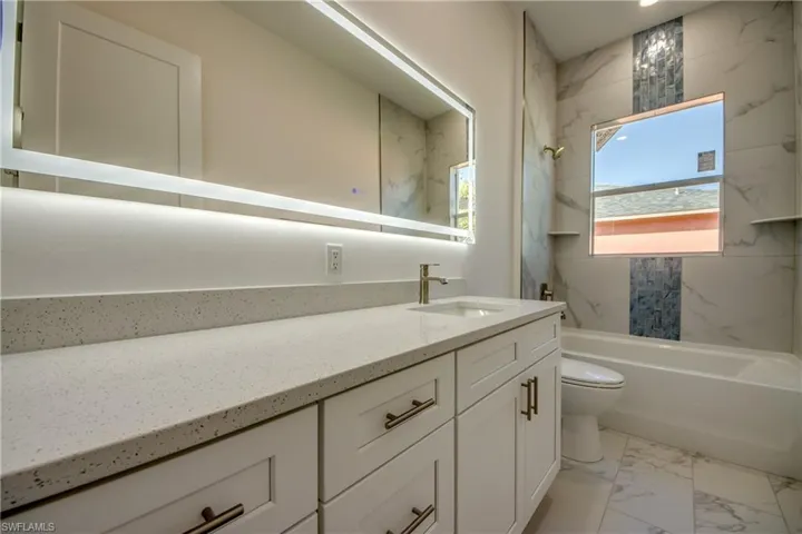 Full bath with light marble finish flooring, vanity, and a combined bath / shower with marble appearance
