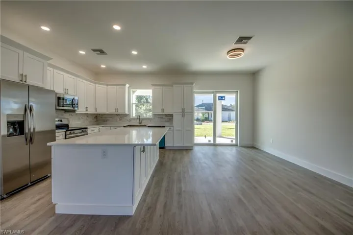 Kitchen with stainless steel appliances, white cabinetry, decorative backsplash, a center island, and recessed lighting