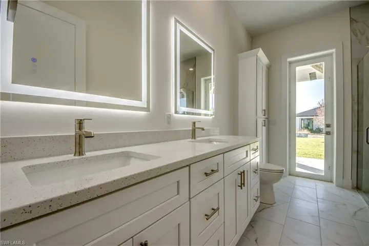 Bathroom with double vanity, light marble finish flooring, and a marble finish shower