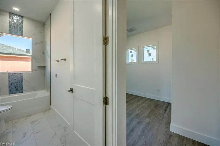 Full bath featuring healthy amount of natural light, tub / shower combination, and light marble finish flooring