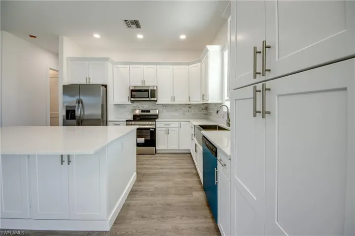 Kitchen featuring stainless steel appliances, white cabinetry, decorative backsplash, recessed lighting, and light stone counters