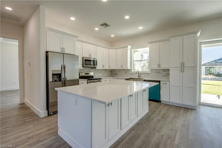 Kitchen featuring white cabinets, appliances with stainless steel finishes, recessed lighting, tasteful backsplash, and a kitchen island