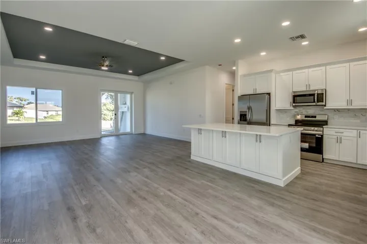Kitchen with white cabinets, stainless steel appliances, decorative backsplash, open floor plan, and recessed lighting