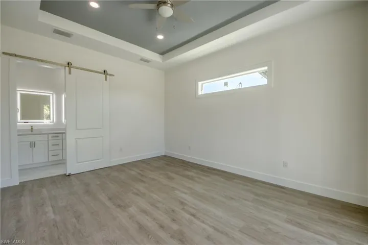 Unfurnished bedroom featuring a barn door, light wood-type flooring, recessed lighting, a raised ceiling, and a ceiling fan