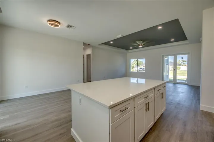 Kitchen featuring open floor plan, a raised ceiling, white cabinets, a center island, and light wood-style flooring