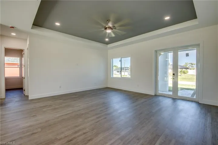 Empty room featuring a raised ceiling, plenty of natural light, wood finished floors, and recessed lighting