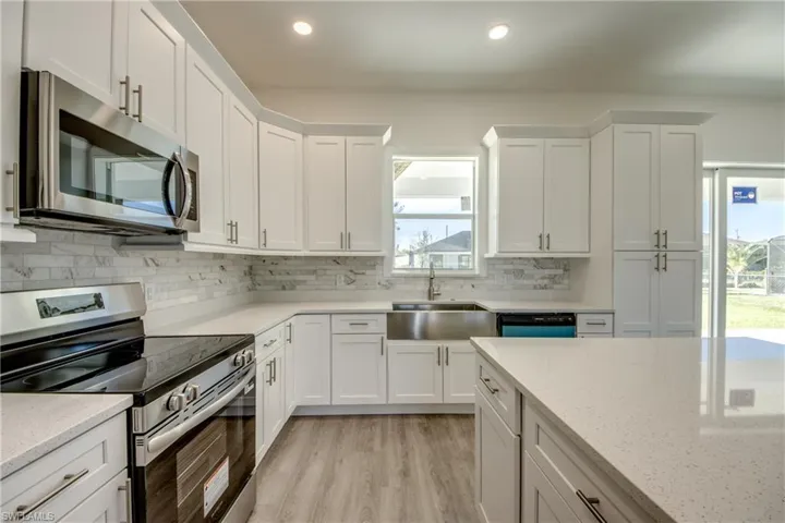 Kitchen with appliances with stainless steel finishes, white cabinets, light wood-style floors, backsplash, and recessed lighting