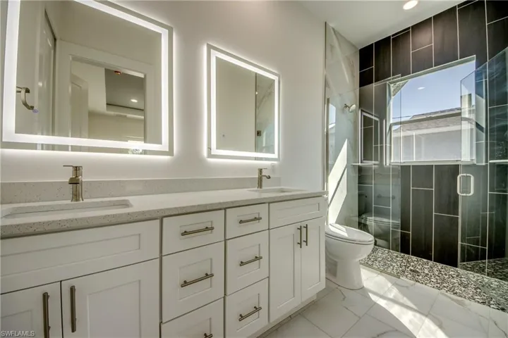 Bathroom with double vanity, a stall shower, light marble finish floors, and recessed lighting