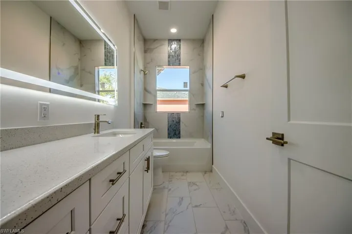 Full bathroom with light marble finish flooring, vanity, and a combined bath / shower with marble appearance